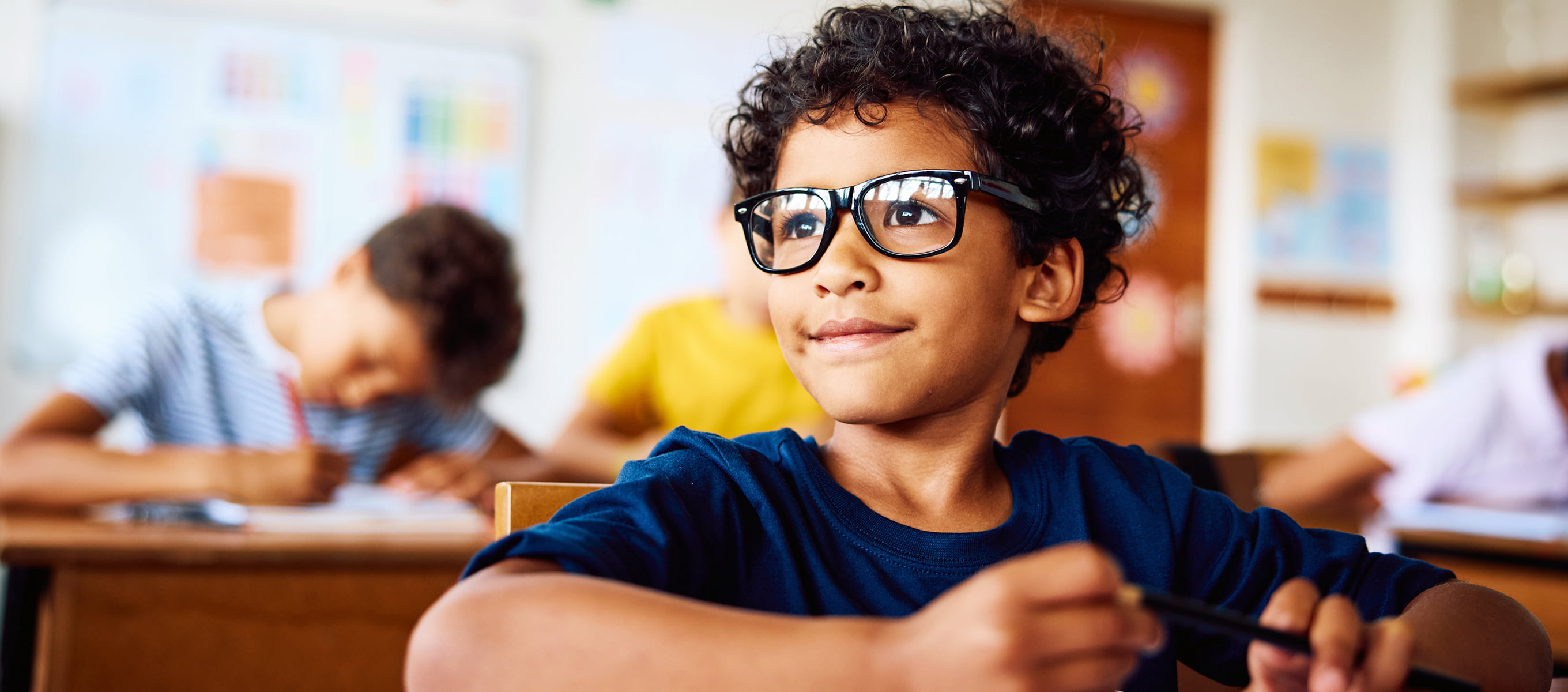 Young student wearing glasses looks up attentively while sitting at a classroom desk