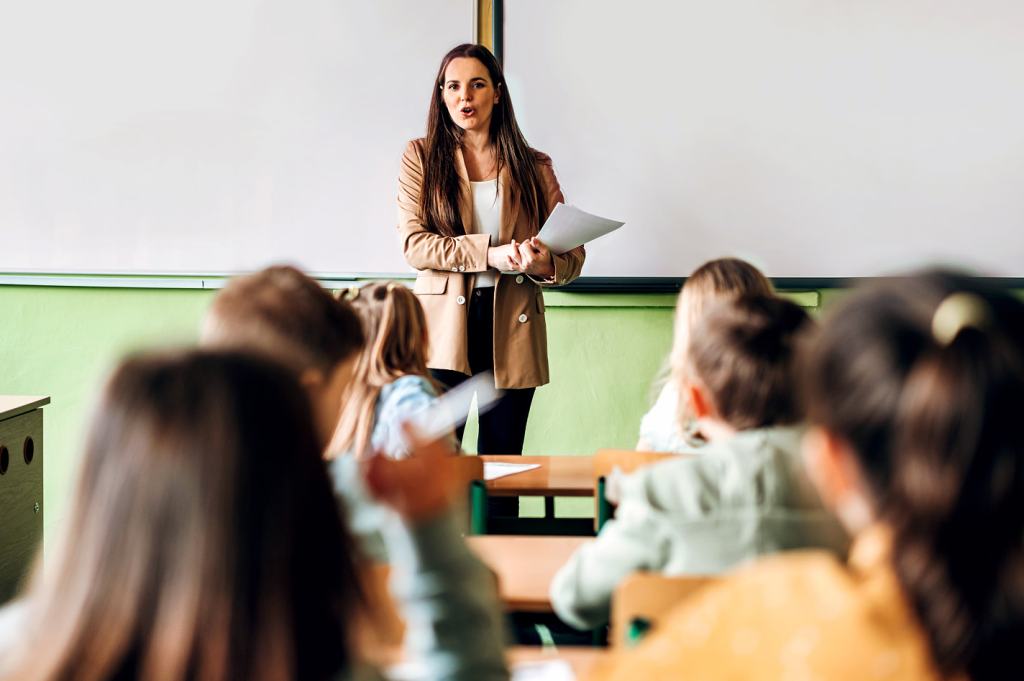 Teacher standing at the front of a classroom addresses seated students