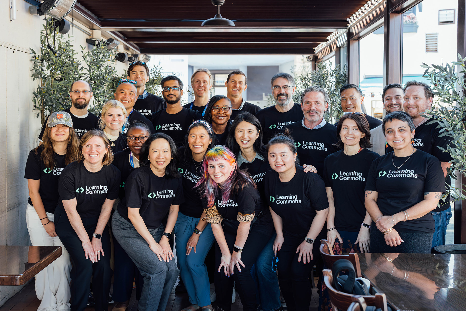 A large group of people posing together wearing black t-shirts displaying the Learning Commons logo